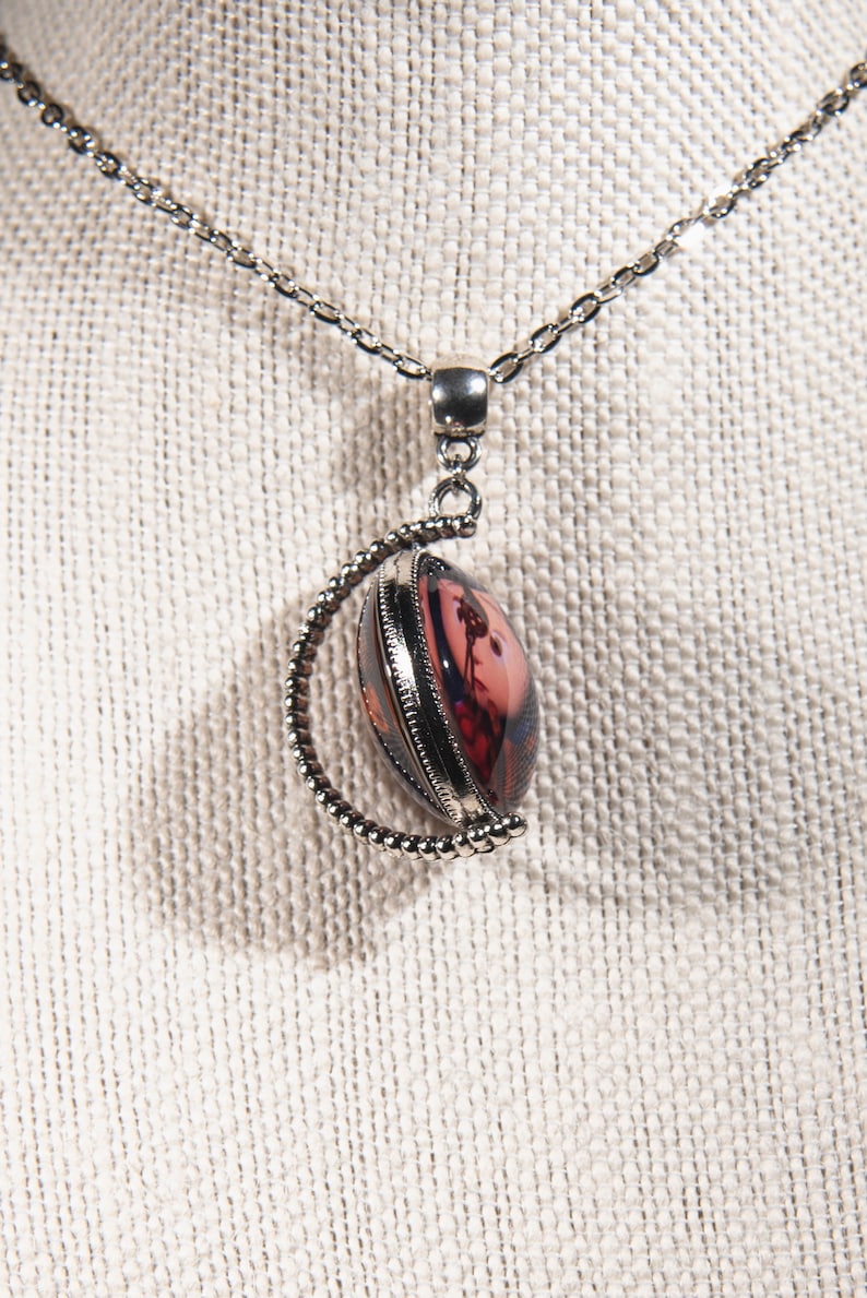 Puede incluir: Un collar de cadena de plata con un colgante redondo que presenta un dise&ntilde;o floral rosa y rojo. El colgante est&aacute; enmarcado en plata y tiene un borde de cuentas.