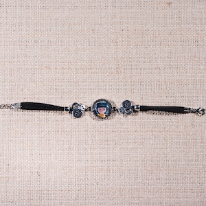 Peut inclure: Un bracelet en cuir noir avec une cha&icirc;ne argent&eacute;e et un charme repr&eacute;sentant une fille de dessin anim&eacute;. Le charme est rond et a une bordure argent&eacute;e.