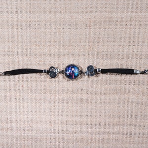 Peut inclure: Un bracelet noir avec un charme argent&eacute; repr&eacute;sentant une image color&eacute;e d'une personne. Le bracelet a un fermoir argent&eacute;.