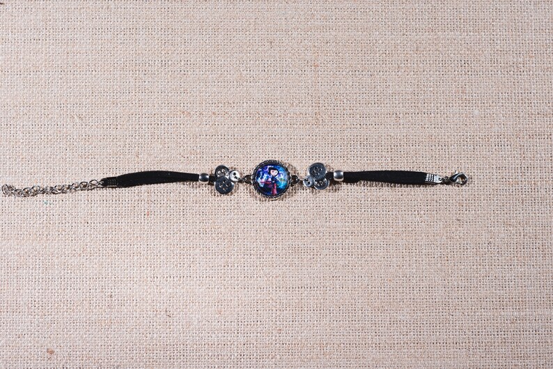 Peut inclure: Un bracelet noir avec un charme argent&eacute; repr&eacute;sentant une image color&eacute;e d'une personne. Le bracelet a un fermoir argent&eacute;.