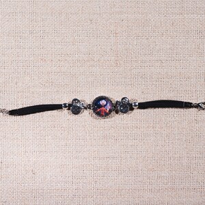 Peut inclure: Un bracelet en cuir noir avec un charme argent&eacute; repr&eacute;sentant un personnage de dessin anim&eacute;. Le charme est rond et pr&eacute;sente une image color&eacute;e d'une fille avec une robe rouge et un fond bleu.
