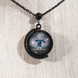 K&ouml;nnte beinhalten: Schwarze Metall-Anh&auml;nger-Halskette mit einem runden Anh&auml;nger mit einem Miniaturgem&auml;lde eines Jungen in einem blauen Anzug. Der Anh&auml;nger h&auml;ngt an einer schwarzen Kette. Der Junge h&auml;lt einen roten Gegenstand.