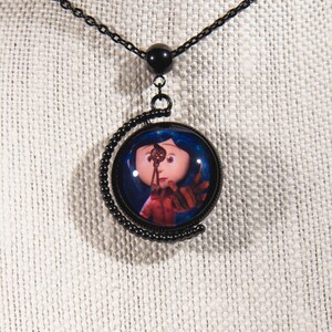 Puede incluir: Collar negro con un colgante redondo de vidrio que presenta un personaje de la pel&iacute;cula "Coraline". El personaje es una ni&ntilde;a con cabello azul y un vestido rojo, sosteniendo una llave.