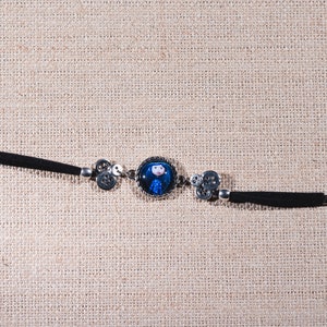Peut inclure: Un bracelet noir et argent avec un charme rond repr&eacute;sentant une fille de dessin anim&eacute; aux cheveux bleus. Le charme est entour&eacute; d'un cadre argent&eacute;.