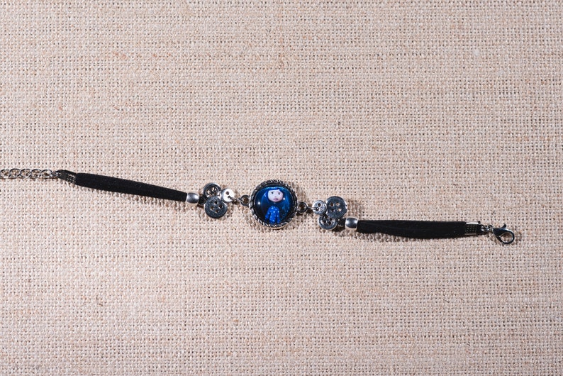 Peut inclure: Un bracelet noir et argent avec un charme rond repr&eacute;sentant une fille de dessin anim&eacute; aux cheveux bleus. Le charme est entour&eacute; d'un cadre argent&eacute;.