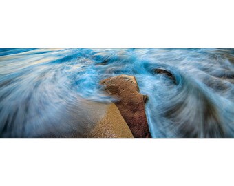 Panoramic photograph of blue swirl waves and crashing surf around a rock at the ocean shore.  Size 12 x 36  inch art photograph.
