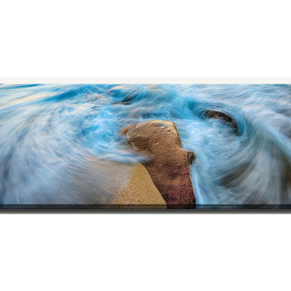 Blue swirling ocean waves and crashing surf around a rock at the shore.  Canvas wrap panoramic decor photograph.