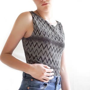 May include: A sleeveless top with a black and silver chevron pattern. The top is made of a shiny, textured fabric.