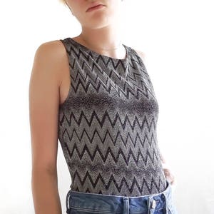 May include: A silver and black sleeveless top with a chevron pattern. The top is made of a sparkly fabric.