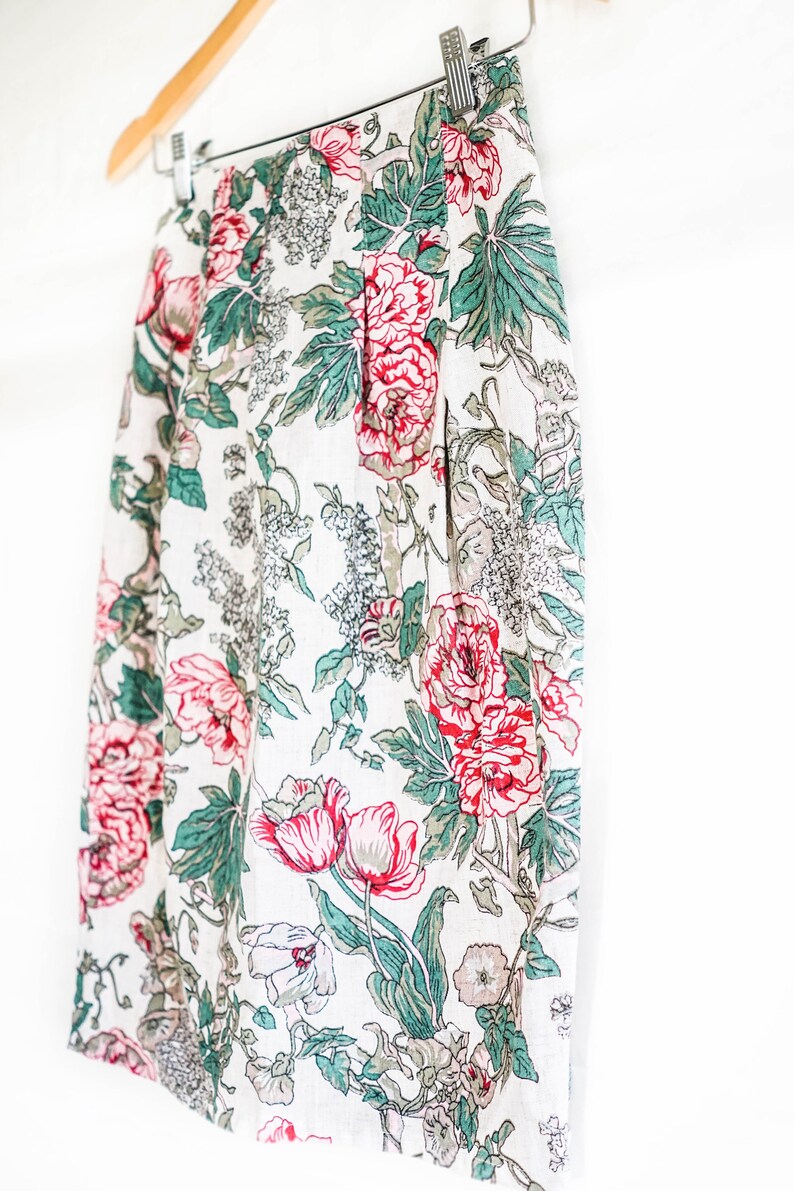 May include: A white skirt with a floral print featuring red, pink, and green flowers. The skirt is made of a lightweight fabric and has a pleated design.