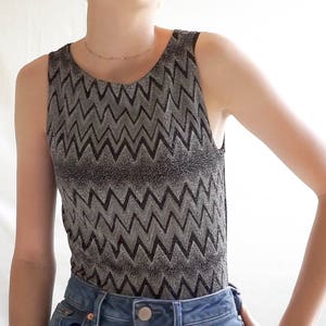 May include: A sleeveless top with a black and silver chevron pattern. The top is made of a shiny, textured fabric.
