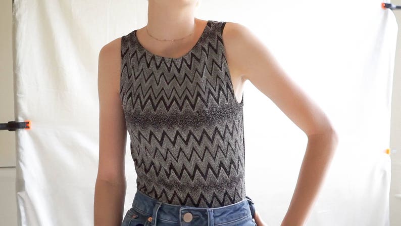 May include: A sleeveless top with a black and silver chevron pattern. The top is made of a shiny, textured fabric.