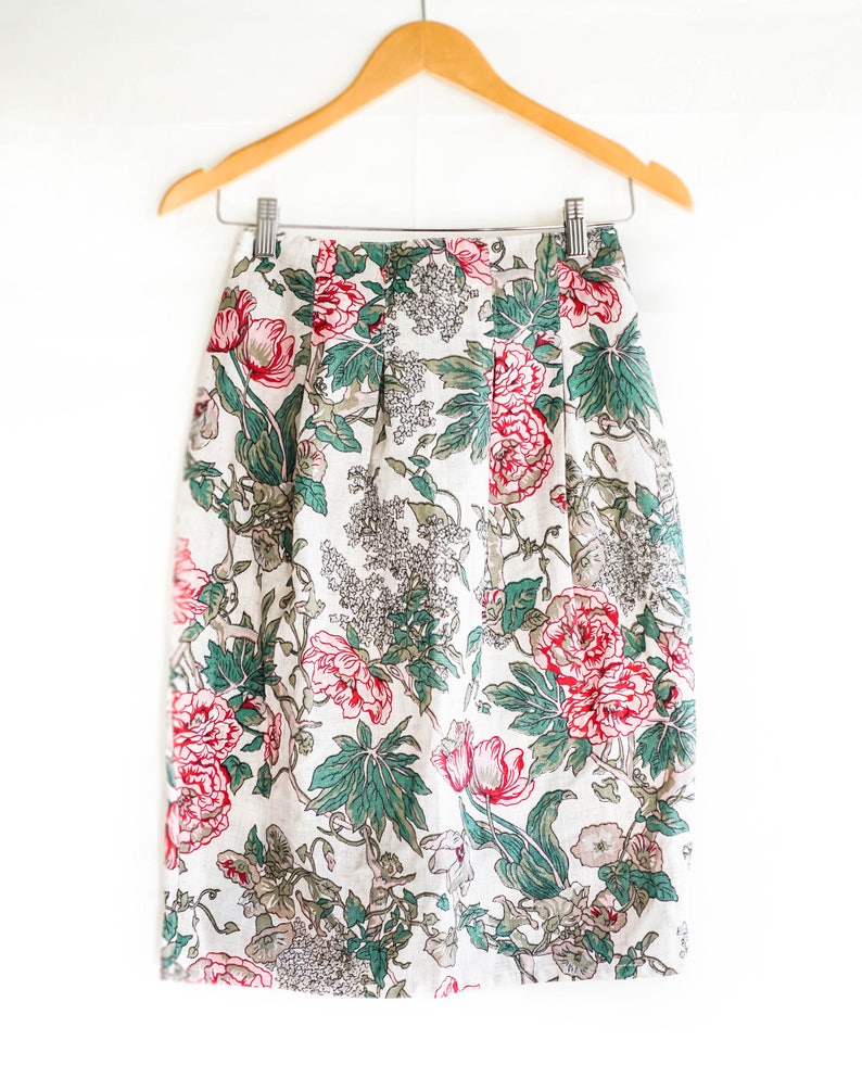 May include: A white skirt with a floral print featuring pink and red flowers and green leaves.