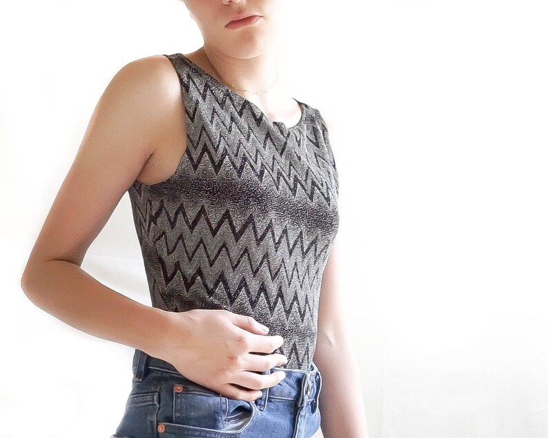 May include: A sleeveless top with a black and silver chevron pattern. The top is made of a shiny, textured fabric.