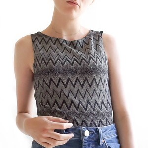 May include: A sleeveless top with a black and silver chevron pattern. The top is made of a shiny, sparkly fabric.
