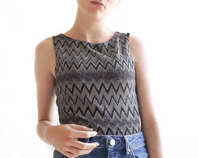 May include: A sleeveless top with a black and silver chevron pattern. The top is made of a shiny, sparkly fabric.