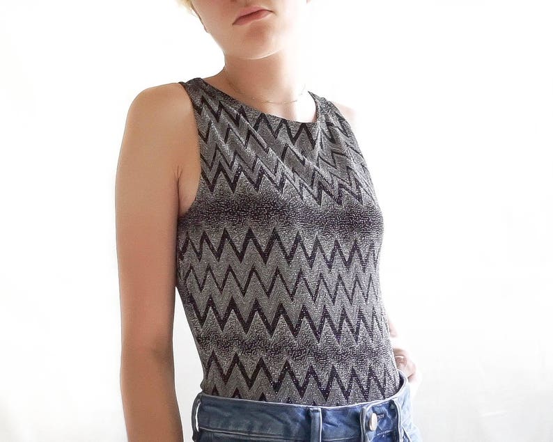 May include: A silver and black sleeveless top with a chevron pattern. The top is made of a sparkly fabric.