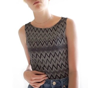 May include: A sleeveless top with a black and silver chevron pattern. The top is made of a shiny, metallic fabric.
