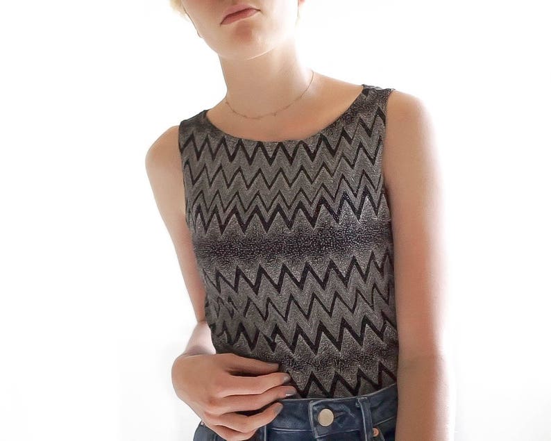 May include: A sleeveless top with a black and silver chevron pattern. The top is made of a shiny, metallic fabric.