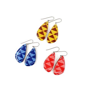 May include: Three pairs of teardrop-shaped earrings with geometric patterns. The earrings are yellow with brown triangles, blue with dark blue triangles, and red with pink triangles.