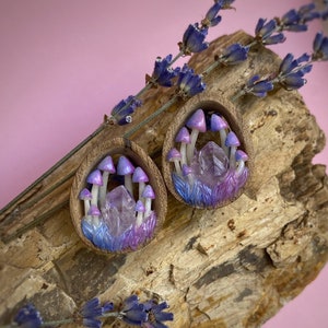 May include: A pair of wooden ear gauges featuring a purple and blue mushroom and crystal design.