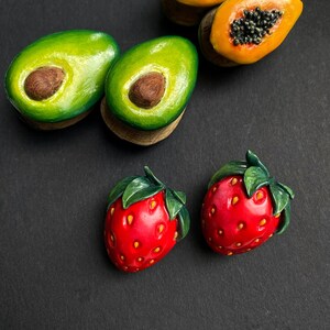 May include: A set of five fruit-shaped earrings, including two avocado halves, two papaya halves, and one strawberry. The earrings are made of polymer clay and have a realistic appearance.