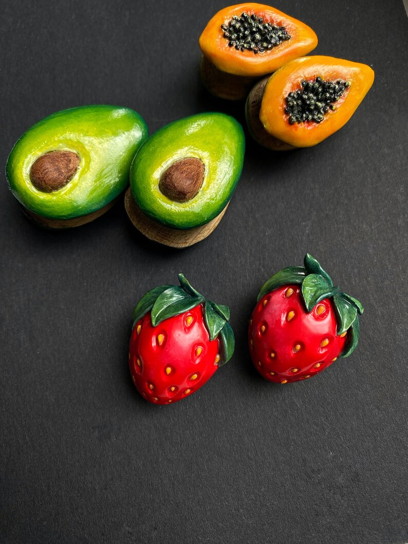 May include: A set of five fruit-shaped earrings, including two avocado halves, two papaya halves, and one strawberry. The earrings are made of polymer clay and have a realistic appearance.