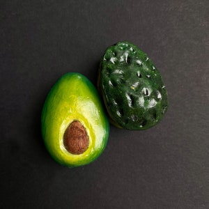 May include: Two halves of an avocado, one cut open to reveal the seed, on a black background.