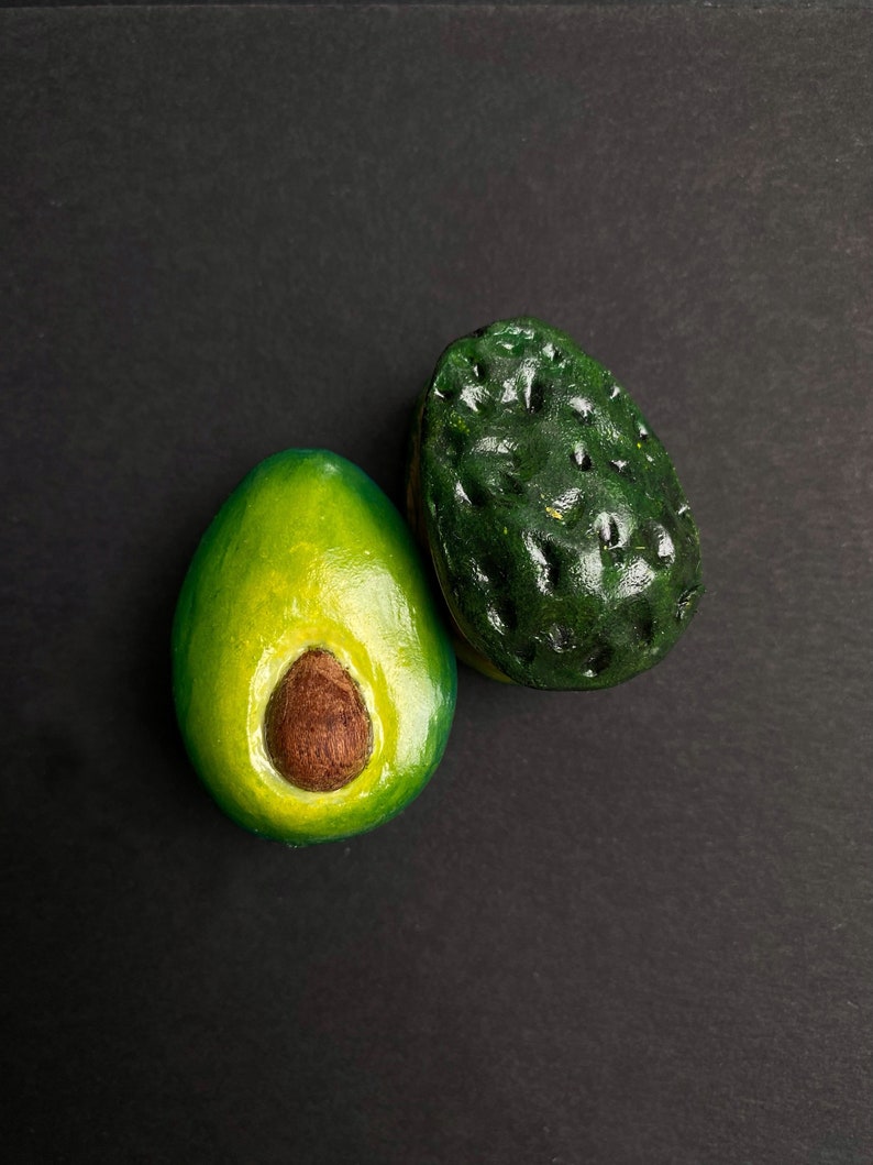 May include: Two halves of an avocado, one cut open to reveal the seed, on a black background.