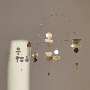 The photo shows a gold-colored brass kinetic mobile. the mobile is made of geometric circles, semicircles and ellipses of different shapes. the figures are connected using thin brass arches. mobile is suspended from the ceiling using a metal chain