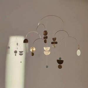 The photo shows a gold-colored brass kinetic mobile. the mobile is made of geometric circles, semicircles and ellipses of different shapes. the figures are connected using thin brass arches. mobile is suspended from the ceiling using a metal chain