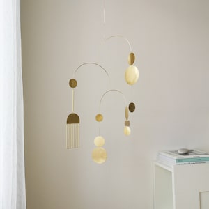 Gold kinetic mobile suspended from the ceiling by the chain. Mobile is made of brass and consists of three thin tube arches on which flat elements of different shapes hang: circles, semicircles and ellipses. Approximate mobile size 24x19 inches