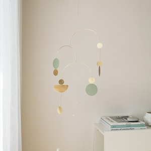 Gold kinetic mobile suspended from the ceiling by the chain. Mobile is made of brass and consists of three thin tube arches on which flat elements of different shapes hang: circles, semicircles and ellipses. Approximate mobile size 22x16 inches