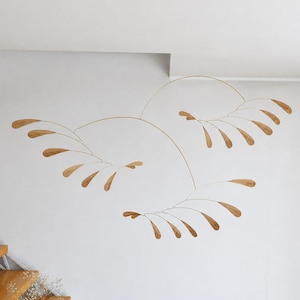 May include: A hanging mobile featuring thin, curved metal wires that support multiple small, flat, wooden leaf-shaped elements. The structure is arranged in three distinct, branching sections that extend outward from a central point.