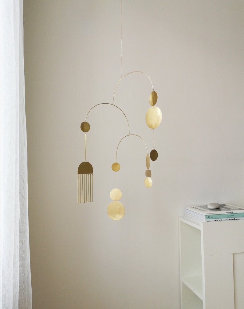 Gold kinetic mobile suspended from the ceiling by the chain. Mobile is made of brass and consists of three thin tube arches on which flat elements of different shapes hang: circles, semicircles and ellipses. Approximate mobile size 24x19 inches