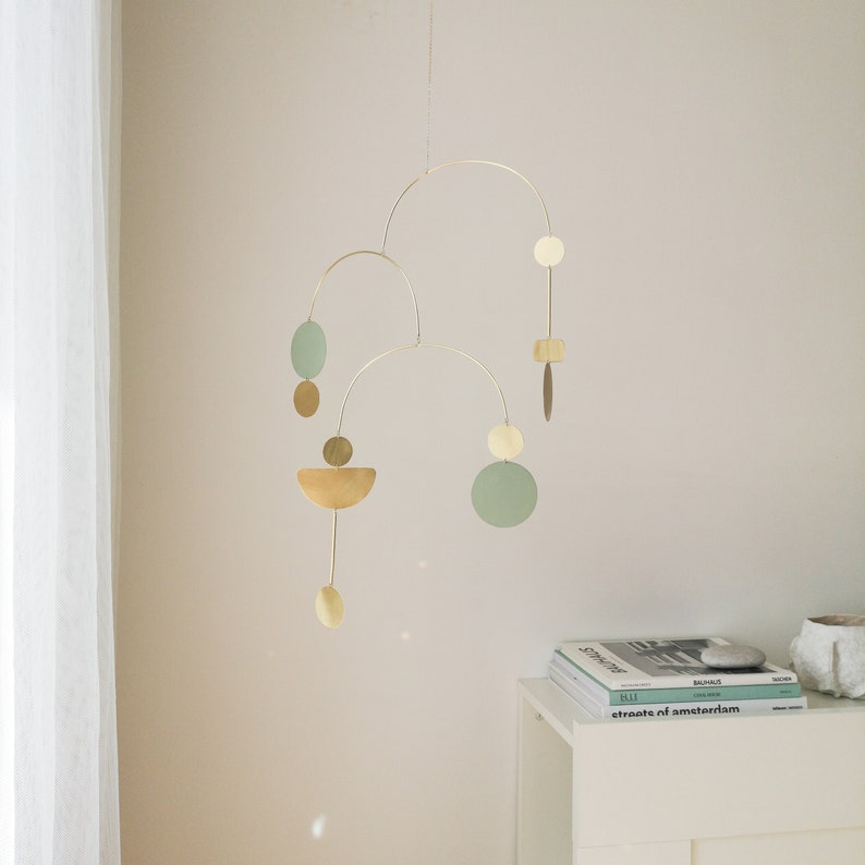 Gold kinetic mobile suspended from the ceiling by the chain. Mobile is made of brass and consists of three thin tube arches on which flat elements of different shapes hang: circles, semicircles and ellipses. Approximate mobile size 22x16 inches