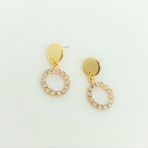 May include: A pair of gold earrings with a small round disc and a circle of clear rhinestones dangling from each.