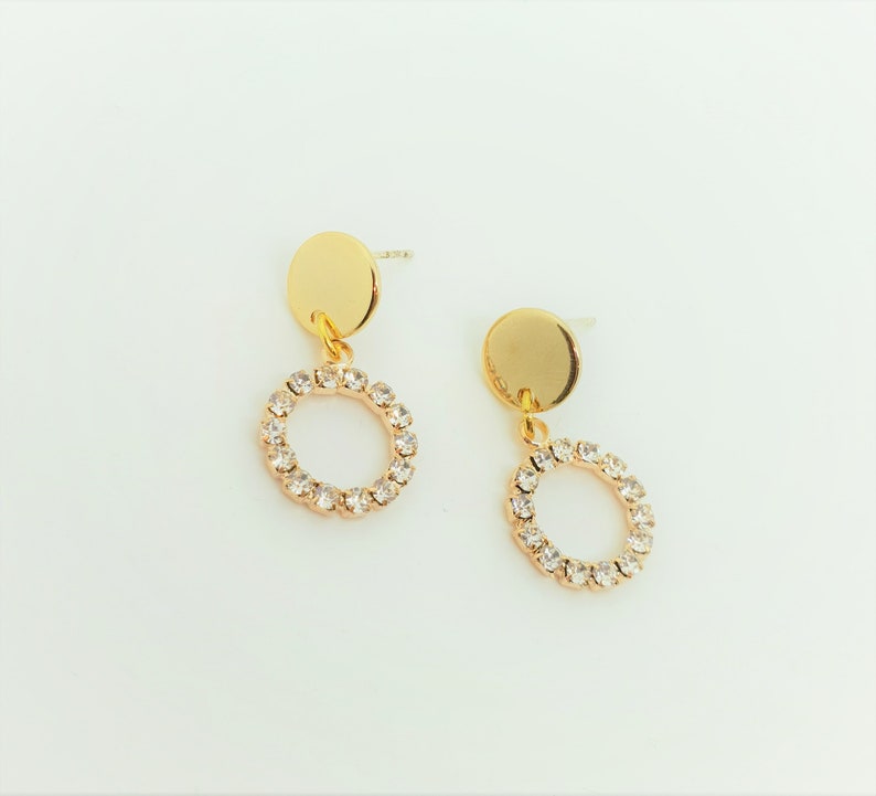May include: A pair of gold earrings with a small round disc and a circle of clear rhinestones dangling from each.
