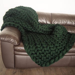 May include: A dark green chunky knit throw blanket draped over a brown leather sofa.