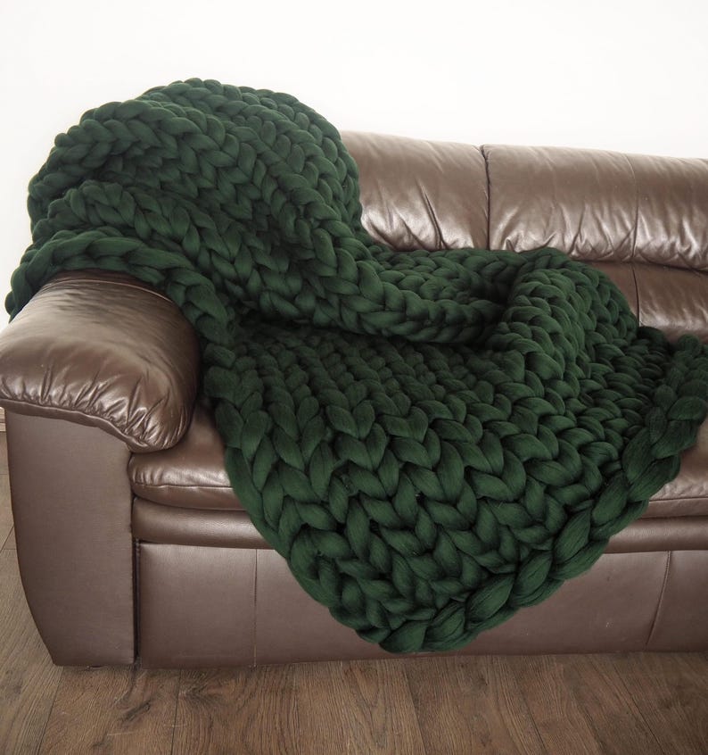 May include: A dark green chunky knit throw blanket draped over a brown leather sofa.
