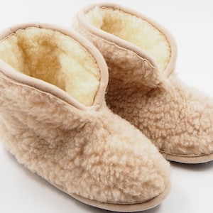 May include: A pair of beige sheepskin slippers with a fluffy texture. The slippers have a closed toe and a short ankle height.