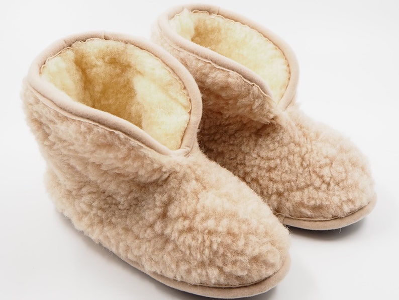 May include: A pair of beige sheepskin slippers with a fluffy texture. The slippers have a closed toe and a short ankle height.