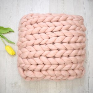 May include: A large, chunky knit throw pillow in a pale pink color. The pillow is made of thick, soft yarn and has a woven texture.