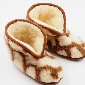 May include: A pair of brown and white sheepskin slippers with a geometric pattern. The slippers are made of soft, fluffy sheepskin and have a brown leather trim.