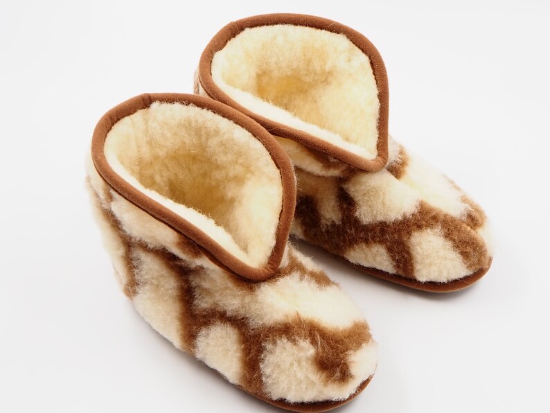May include: A pair of brown and white sheepskin slippers with a geometric pattern. The slippers are made of soft, fluffy sheepskin and have a brown leather trim.