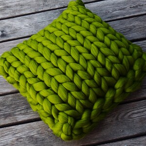 May include: A large, chunky knit pillow in a bright green color. The pillow is made of thick yarn and has a soft, cozy texture.