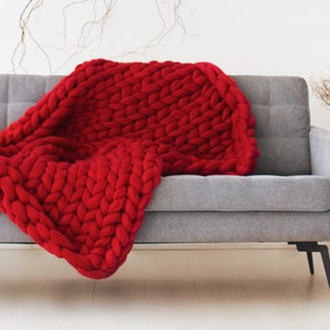 May include: A red chunky knit throw blanket draped over a gray sofa with black legs.