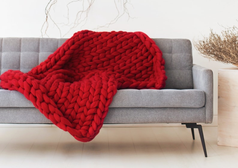 May include: A red chunky knit throw blanket draped over a gray sofa with black legs.