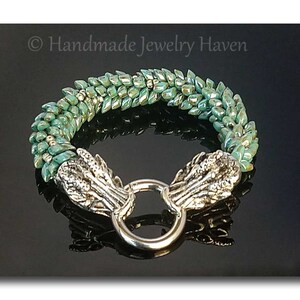 May include: A green and silver beaded bracelet with a silver dragon head clasp. The bracelet is made with small, iridescent beads that create a shimmering effect. The dragon head clasp is detailed and intricate, with a ring for easy fastening.