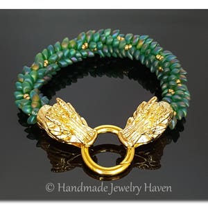 May include: A green beaded bracelet with gold dragon head clasps. The bracelet is made with small, iridescent green beads and features a gold ring connecting the two dragon heads.